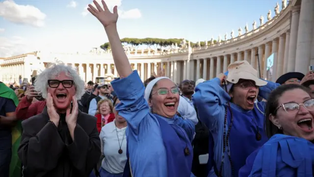 A nun holds up her hand in celebration, while a man next to her shouts with joy