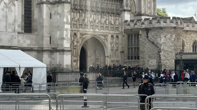 A line of people start to enter Westminster Abbey from the main entrance, a white security tent visible to the far left of the image
