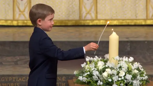 Alexander Churchill in a black suit lights up the candle of peace in Westminster Abbey (cream candle surrounded by white flowers)