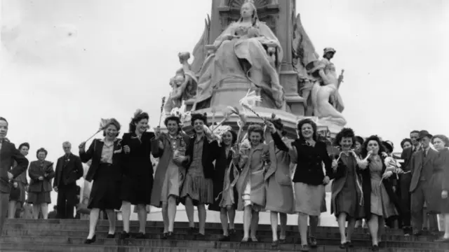 Young girls standing outside Buckingham Palace in front of the statue of Queen Victoria
