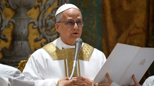 closeup of Pope Leo XIV speaking into the microphone in church, dressed in gold and white vestments.