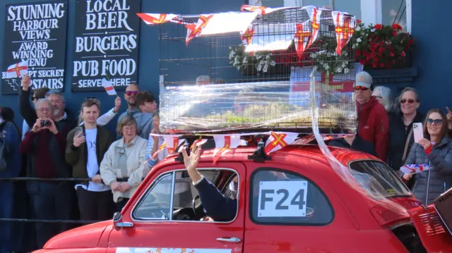 A red VW Beetle with a shrink-wrapped cage on top.