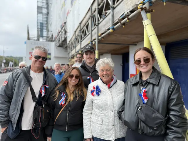 Five people wearing red, white and blue ribbons smiling
