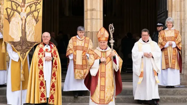 The Archbishop of York Stephen Cottrell (centre) wearing a yellow and red vest and bishop's hat.
