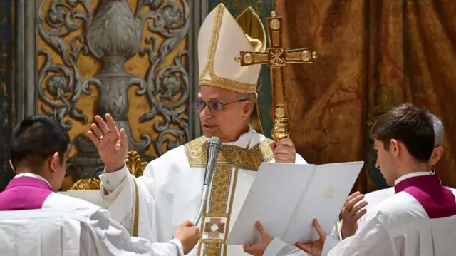 Pope Leo speaks into a microphone, while an altar boy is holding up a book for him to read from