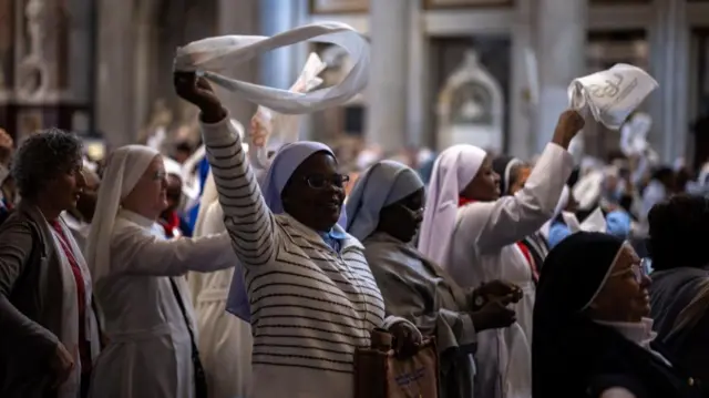 Black nun in foreground twirling a white scarf above her head. More nuns in background doing the same.