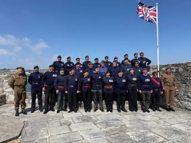 About 30 veterans in blue or khaki military uniforms standing on a castle battlement.
