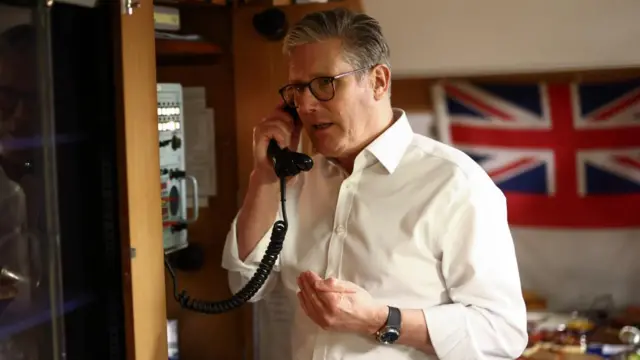 Starmer in a white shirt with sleeves rolled up, speaking on the telephone.