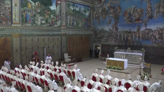 Inside the sistine chapel, caridnals are in white robes and hats