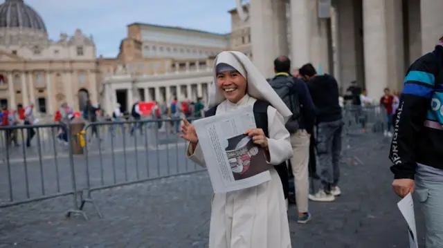 Smiling nun holds a copy of the L'Osservatore Romano newspaper, containing a photograph of newly elected Pope Leo XIV
