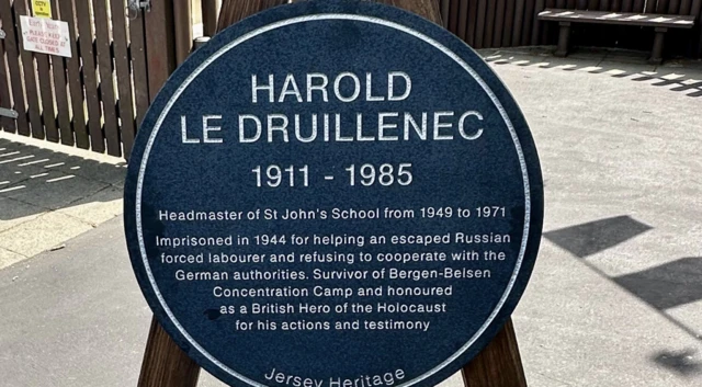 The plaque reads: "HAROLD LE DRUILLENEC 1911-1985 Headmaster of St John's School from 1949 to 1971. Imprisoned in 1944 for helping an escaped Russian forced labourer and refusing to cooperate with German authorities. Survivor of Bergen-Belsen Concentration Camp and honoured as a British Hero of the Holocaust for his actions and testimony. Jersey Heritage."