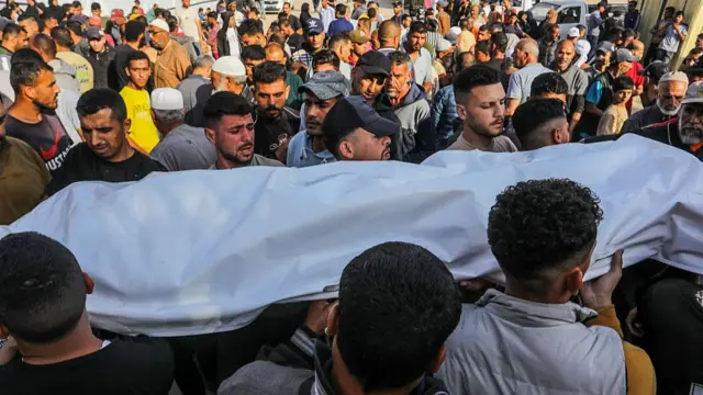 Palestinian men carry a white body bag through a crowd