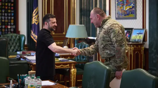 zelensky shakes hands with the head of Ukraine's security service. zelensky wears black, maliuk is dressed in army fatigues.