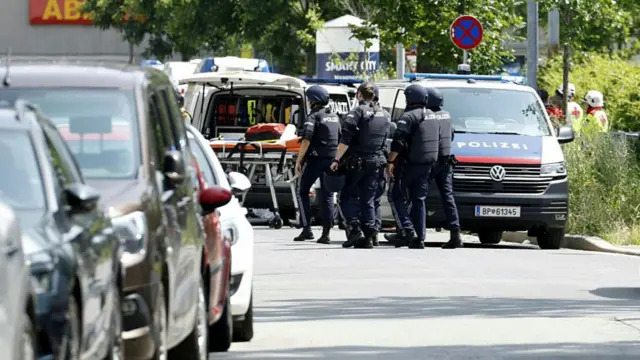 Several police officers walk past an ambulance which has unloaded a stretcher