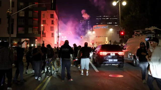 Protestors stand in a road in Los Angeles on Monday night. Smoke is seen in the distance.