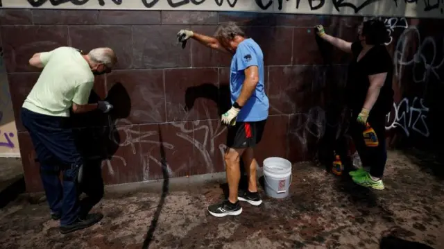 Three people dressed in casual clothing clean up graffiti