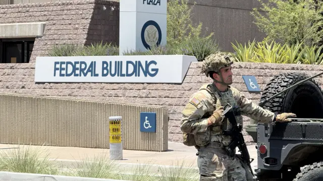 An armed National Guard troop stands by a vehicle in front of a sign that says "federal building".
