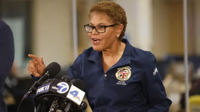 LA Mayor Karen Bass addresses the media from behind several TV microphones