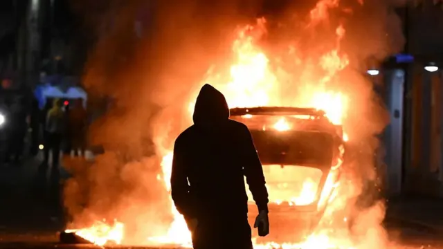 A man standing in front of a car on fire