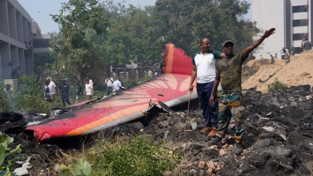 Part of plane on the floor, people stood around.