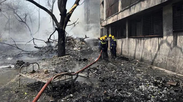 Firefighters beside a smouldering wreckage