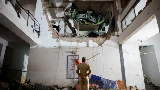 An Indian police officer looks at the plane wreckage stuck between floors of a building in Ahmedabad. Photo: 12 June 2025