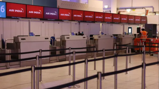 Empty Air India desks at Gatwick Airport, a worker in orange hi-vi vest working to the side behind a plastic orange barrier