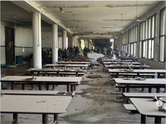 A canteen with tables and benches in the foreground with a large hole in the wall to the rear and what looks like debris from the aircraft