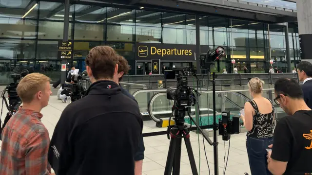 People stand next to cameras outside the departures area at Gatwick
