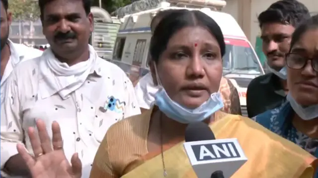 A woman wearing a yellow saree speaks into the mic