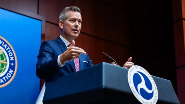 Sean Duffy stands at a podium and gestures with his hands as he speaks at a media briefing