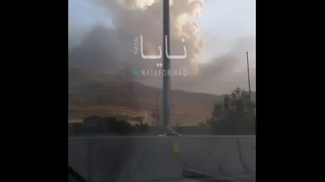 Smoke rising from hills during the day, the image includes a social media watermark.