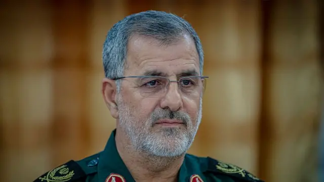 Headshot of Pakpour who looks on past the camera. He has short white stubble and wears glasses