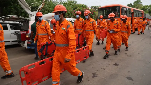A group of men in orange high-vis suits and helmet carry stretchers down the street.