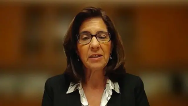 Mona Yacoubian speaks to the camera, a blurred background behind her