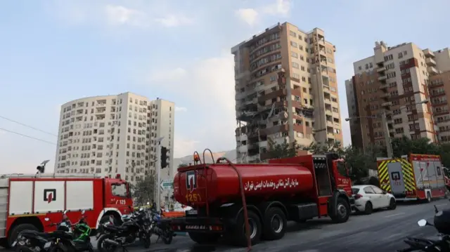 A number of emergency service trucks can be seen on the road with damaged high rise buildings behind them