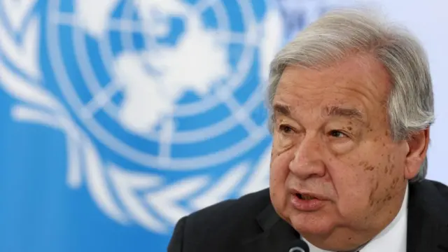 Antonio Guterres, secretary-general of the UN, speaks into a microphone in front of the UN logo.