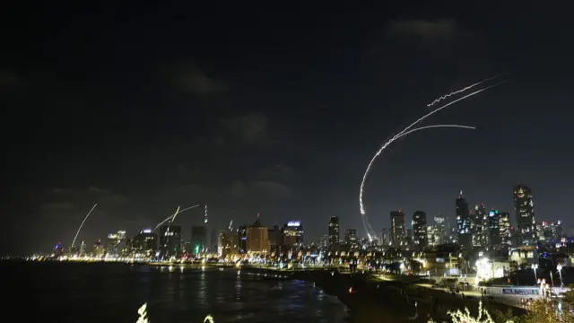 Night picture of the Tel Aviv skyline as Iranian missiles are intercepted in the black sky