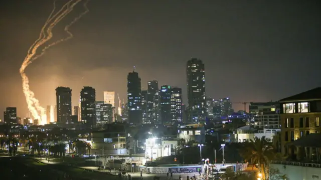 A bright light among buildings in Tel Aviv, with the trail of either a missile or the interception system