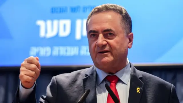Israel Katz in a navy suit and red tie, raising one fist