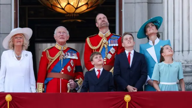 Britain's King Charles, Queen Camilla, Prince William, Prince of Wales, Catherine, Princess of Wales, Prince George, Princess Charlotte and Prince Louis appear on the balcony of Buckingham Palace and all look above.