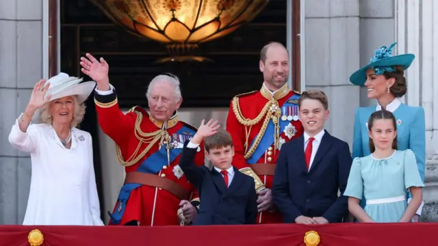 Camilla, Charles, William, Kate and their three children smile and wave on palace balcony.