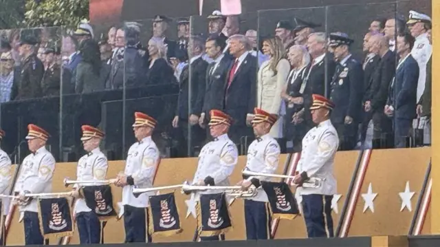 President Trump stands with Melania Trump and other dignitaries in a viewing area