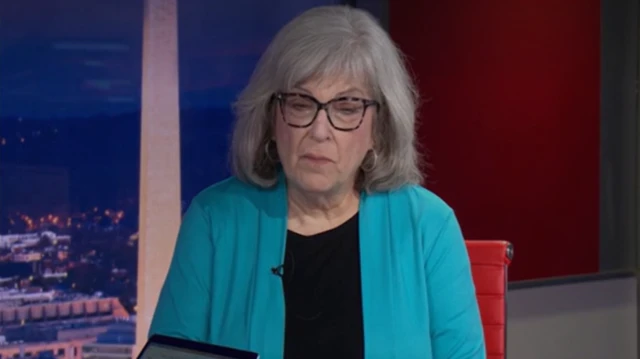 A women wearing a blue blazer sits on set in a BBC studio.