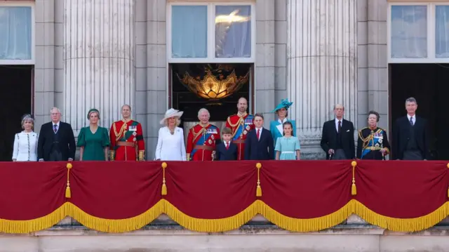 Royal Family members wear formalwear and stand on the balcony at Buckingham Palace.