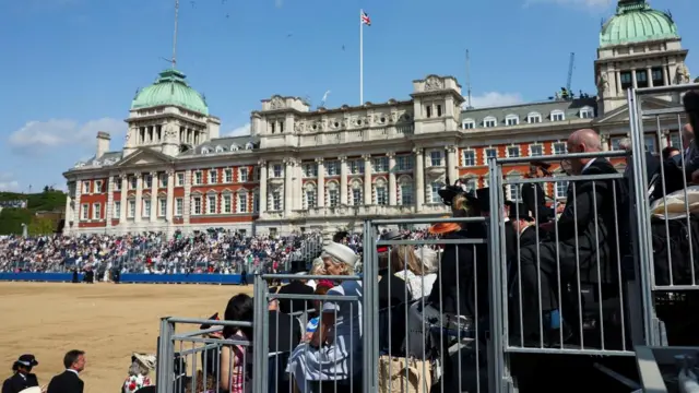 People arrive to witness the Trooping the Colour parade. Crowds of people take their seats.