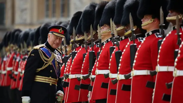Britain's King Charles III, Colonel in Chief of the Coldstream Guards inspects the regiment. Charles is in black uniform and smiles in front of a line of people in Welsh Guards Uniform.