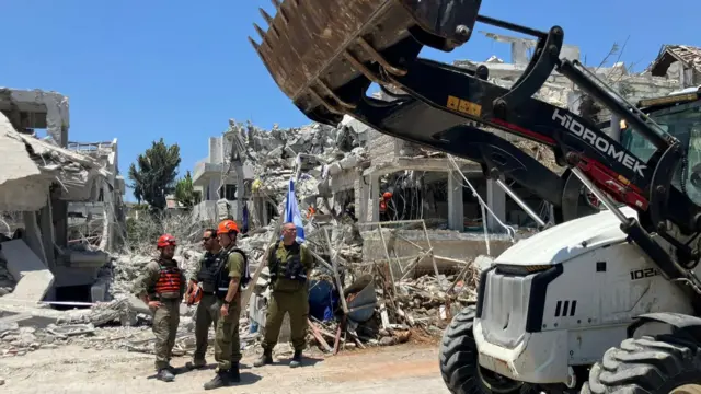 workers stand beside rubble as a truck clears debris