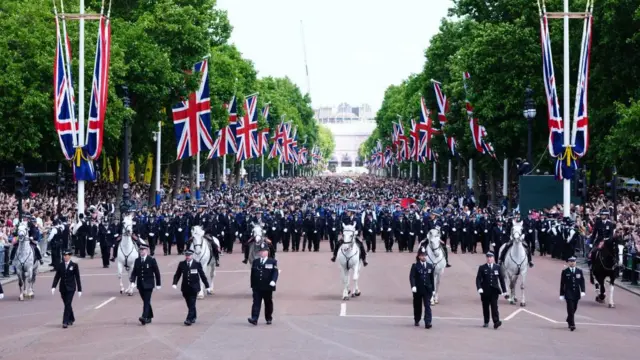 Crowds make their way down the Mall in front of a line of police officers, some on horses.