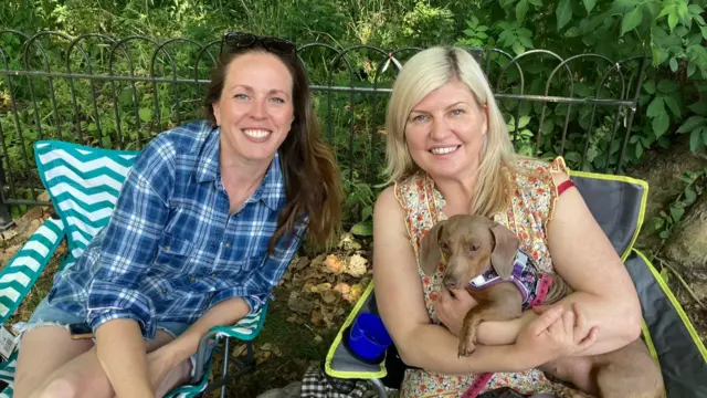 Jodie and Lucy sit on chairs outside, with Lucy holding a small dog.